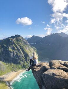 jente sitter på kanten av en klippe og ser på utsikten over strand